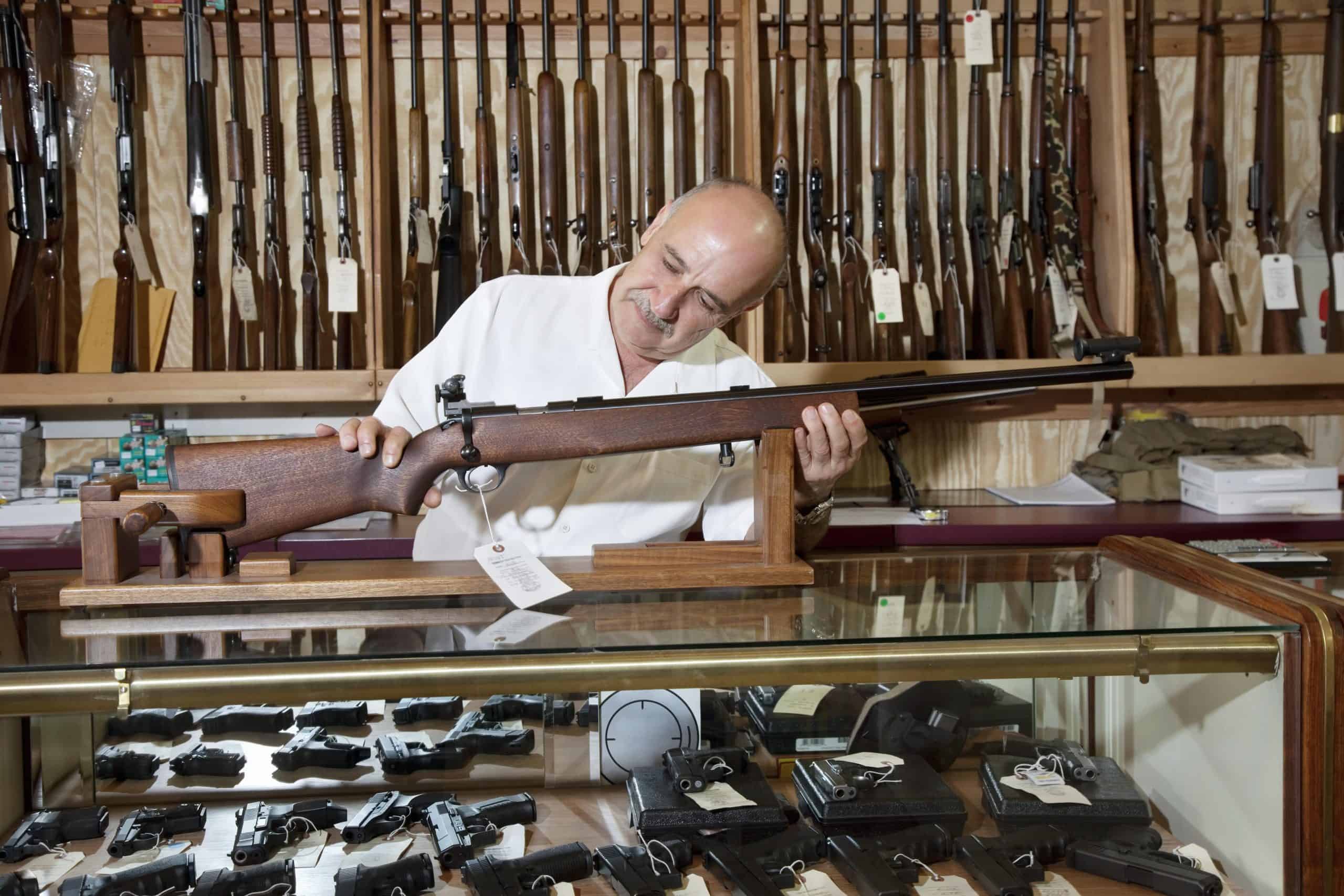 Rhode Island gun store | Mature gun shop owner looking at rifle in store