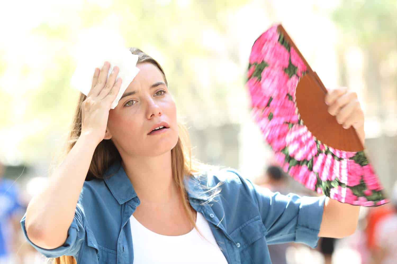 Sad woman fanning and sweating suffering a heat stroke on summer in the street