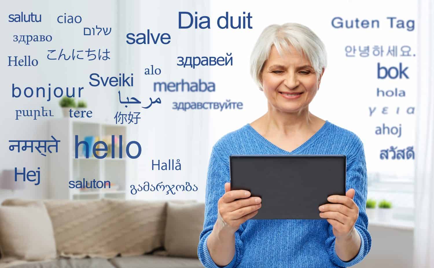 technology, online translator and old people concept - smiling senior woman using tablet computer over greeting words in different foreign languages