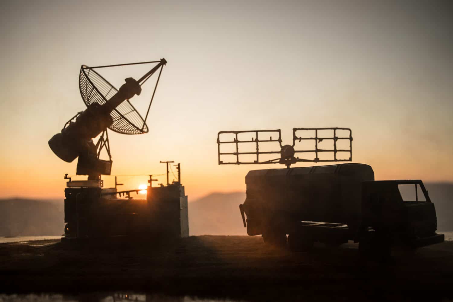 Creative artwork decoration. Silhouette of mobile air defence truck with radar antenna during sunset. Satellite dishes or radio antennas against evening sky. Selective focus