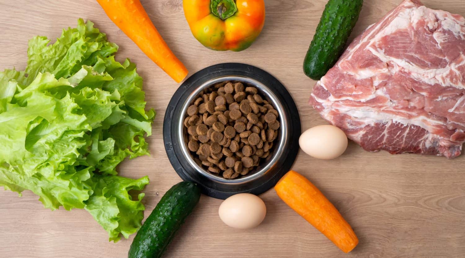 Dry pet dog food with natural ingredients. Raw meat, vegetables, eggs and salad near bowl with dry pet feed on wooden background. concept of a correct balanced and healthy nutrition for pet, flatly