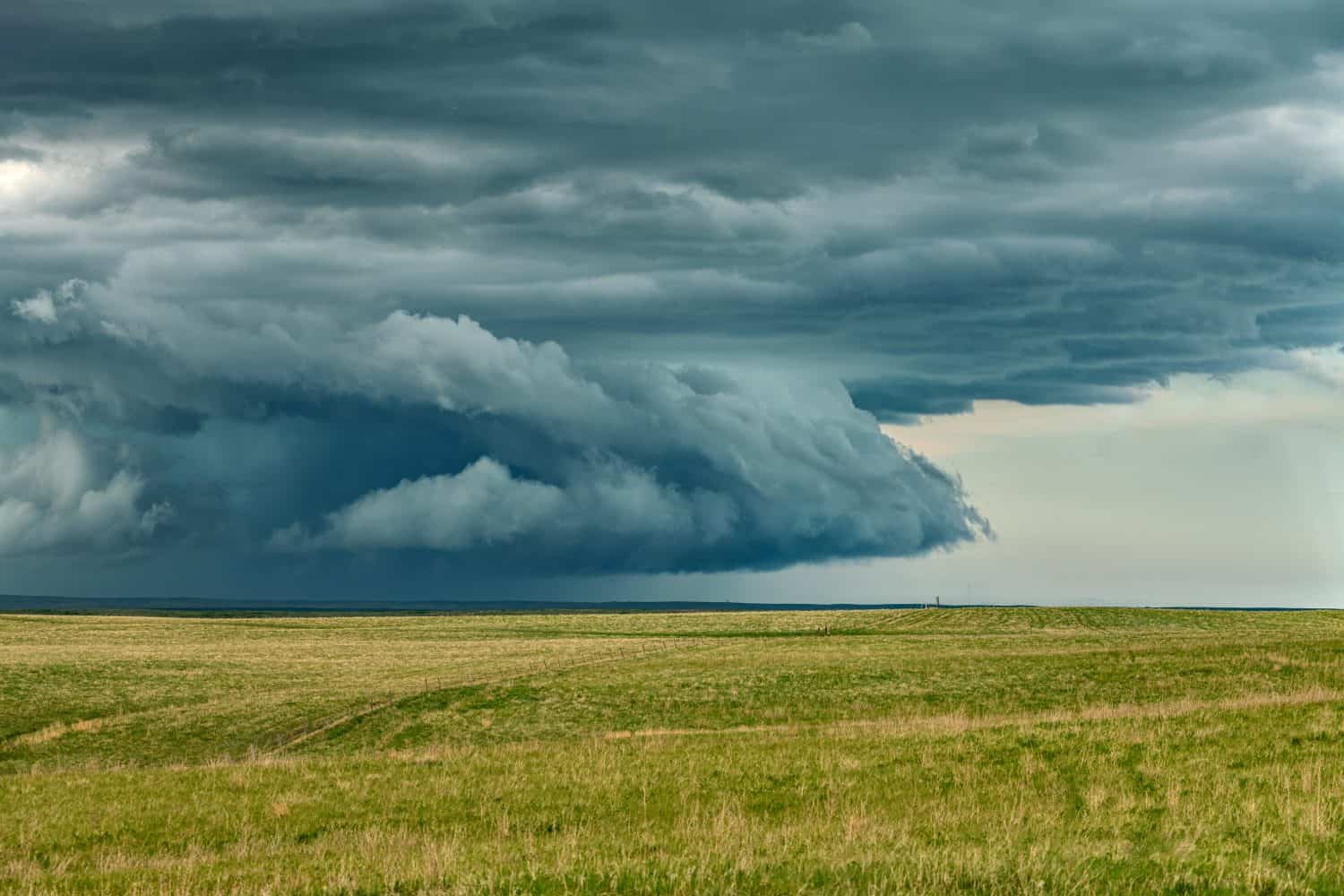 Panorama of a massive mesocyclone weather supercell, which is a pre-tornado stage, passes over a grassy part of the Great Plains while fiercely trying to form a tornado.