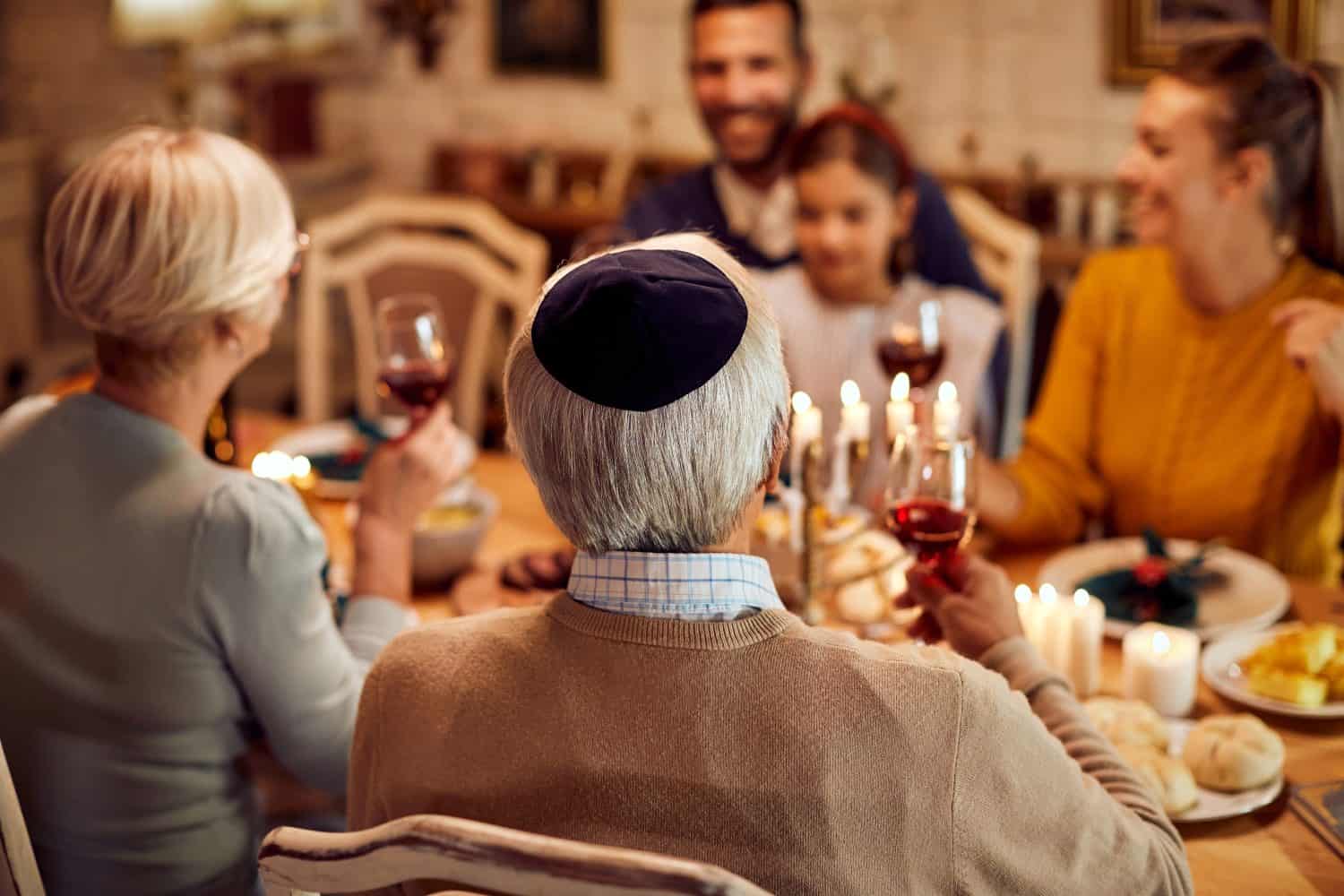 Back view of senior man wearing yarmulke during traditional family meal on Hanukkah.