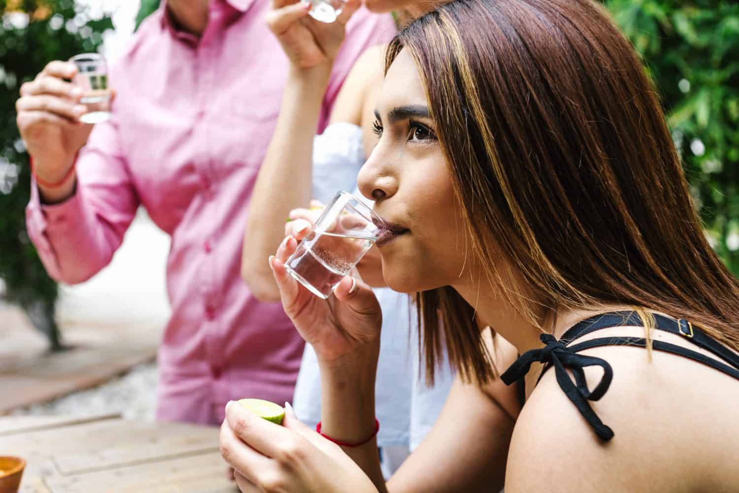 Latin Woman drinking tequila or mezcal shot with group of young latin Friends making A Toast In Restaurant terrace in Mexico Latin America