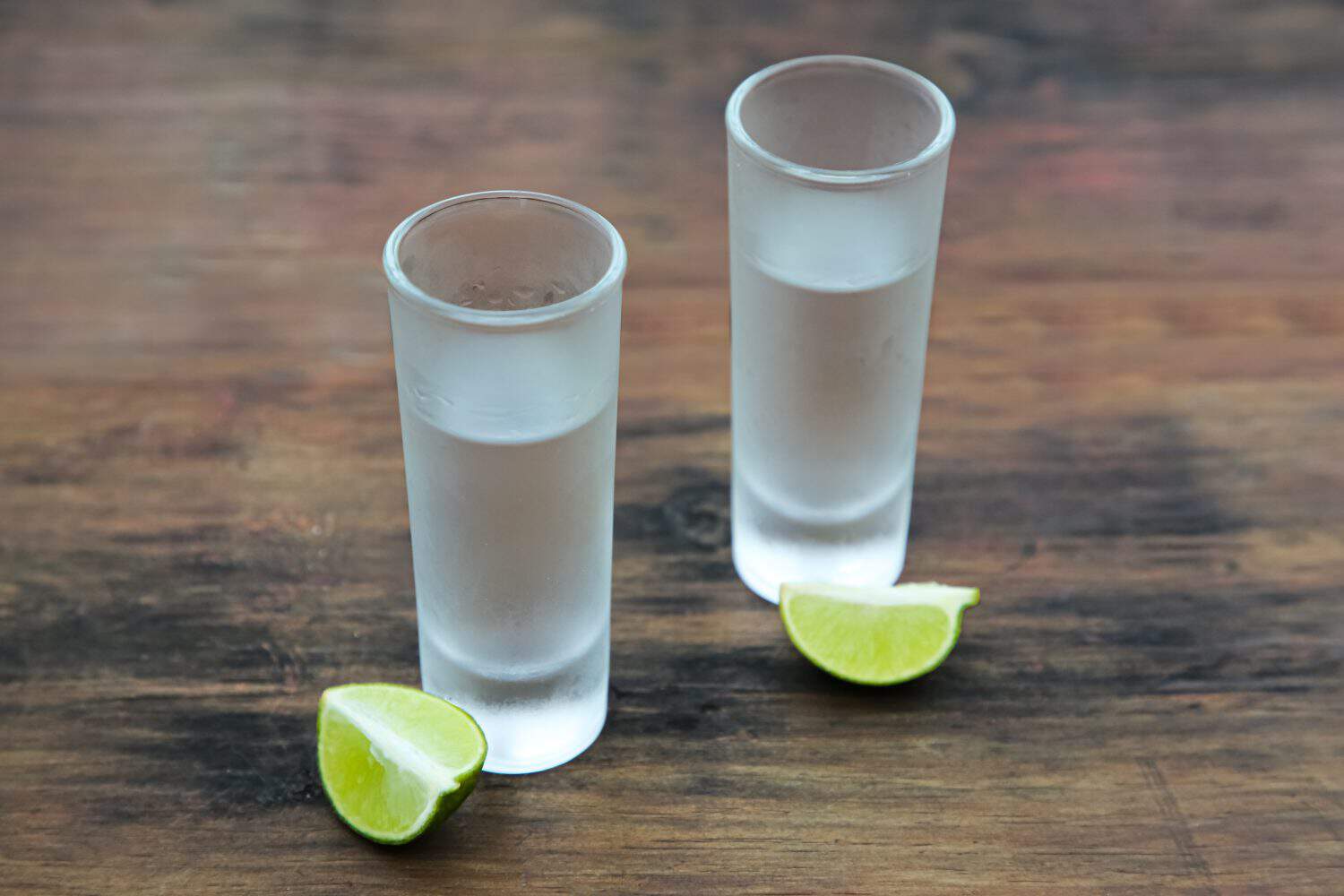 Mexican tequila shots with lime slices on wooden table. Drink made from agave