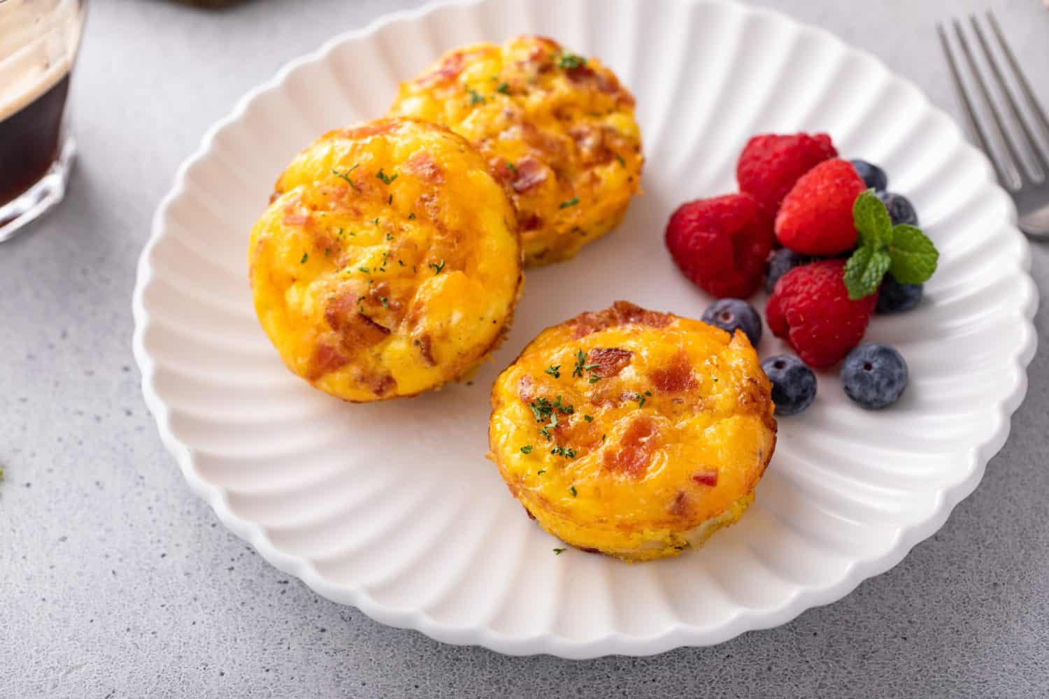 Breakfast egg muffins or egg bites with potato, bacon and cheddar served with fresh berries