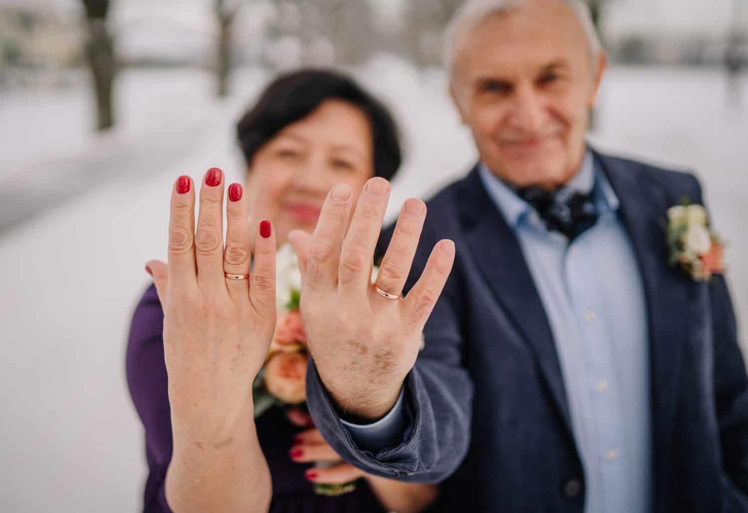 A winter wedding features a radiant senior bride and groom, a mature couple celebrating their love amidst the enchanting backdrop of the season. Showing wedding rings, soft focus