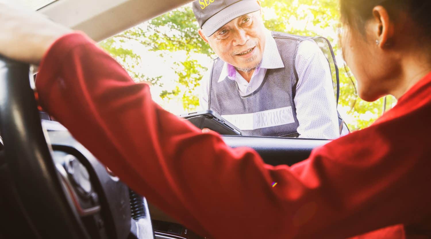 Asian woman driving car asks travel assistance and asks the senior male security guard standing provide friendly and polite service receives assistance in solving immediate problems efficiently.