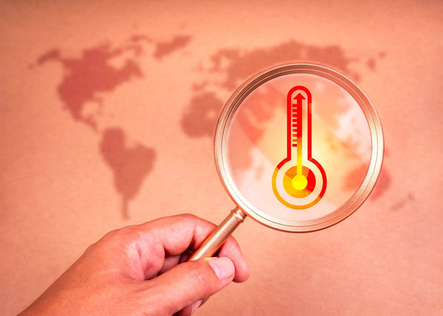 Global warming and greenhouse effect concepts. Close-up of hot degree weather thermometer high temperature icon symbol in magnifying glass lens holding by hand on red background with blur world map.