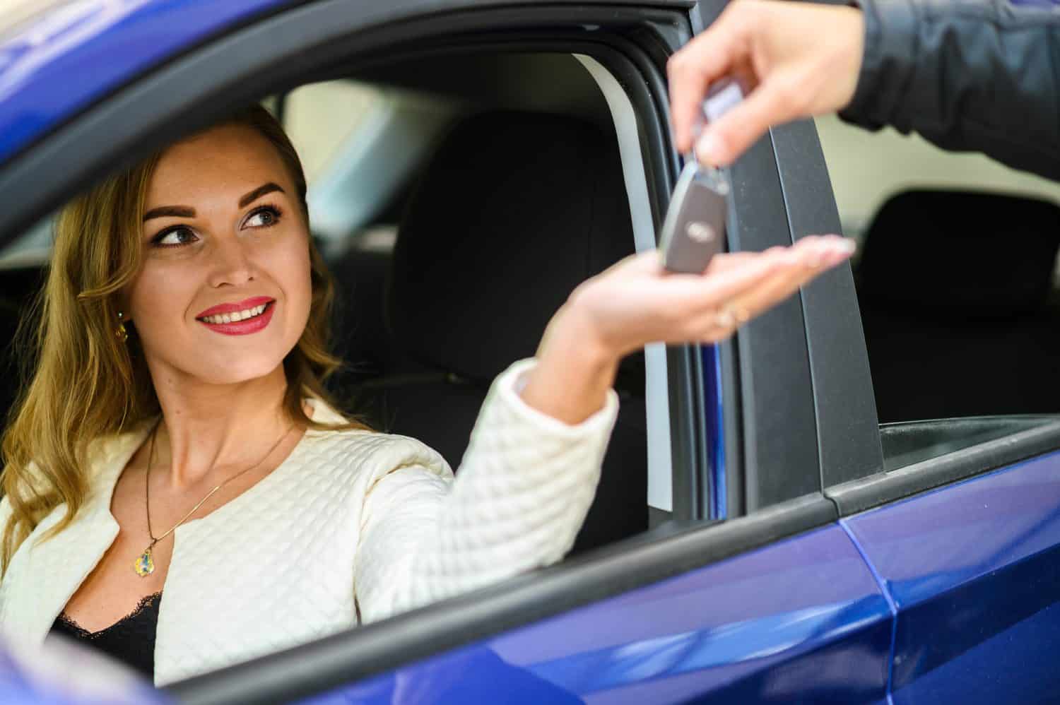 Excited woman receives car keys in bright showroom, ready to drive her new ride