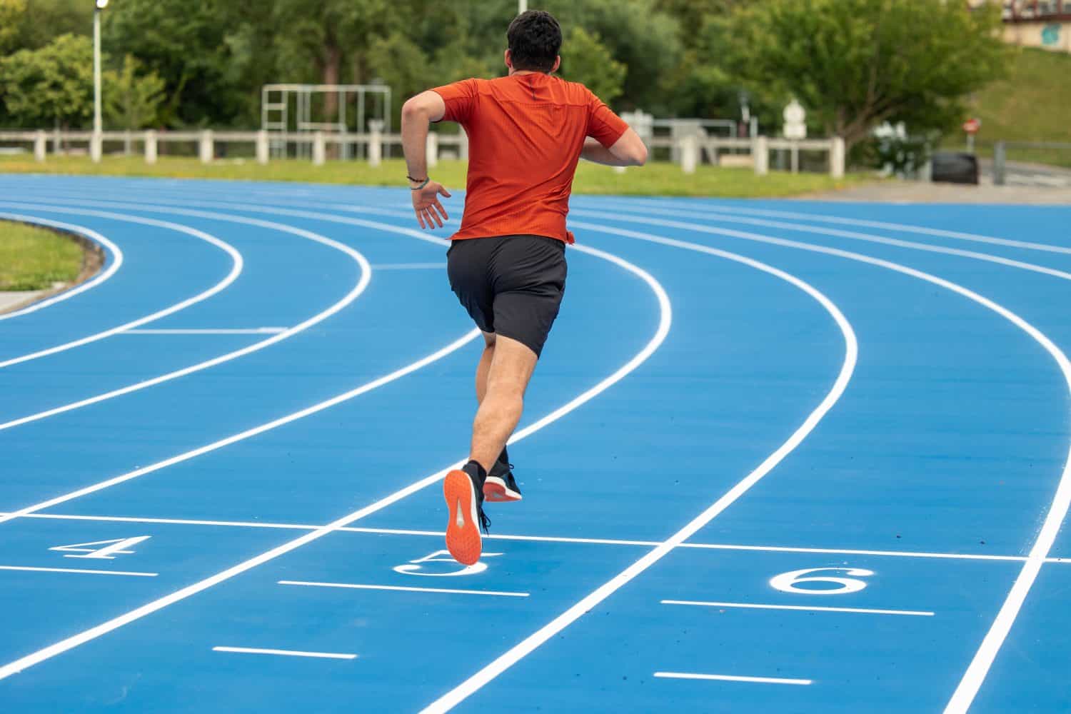 athlete runner is seen from behind while training on a blue athletic track. This image captures the determination and focus of the athlete as they physically and mentally prepare for their competition