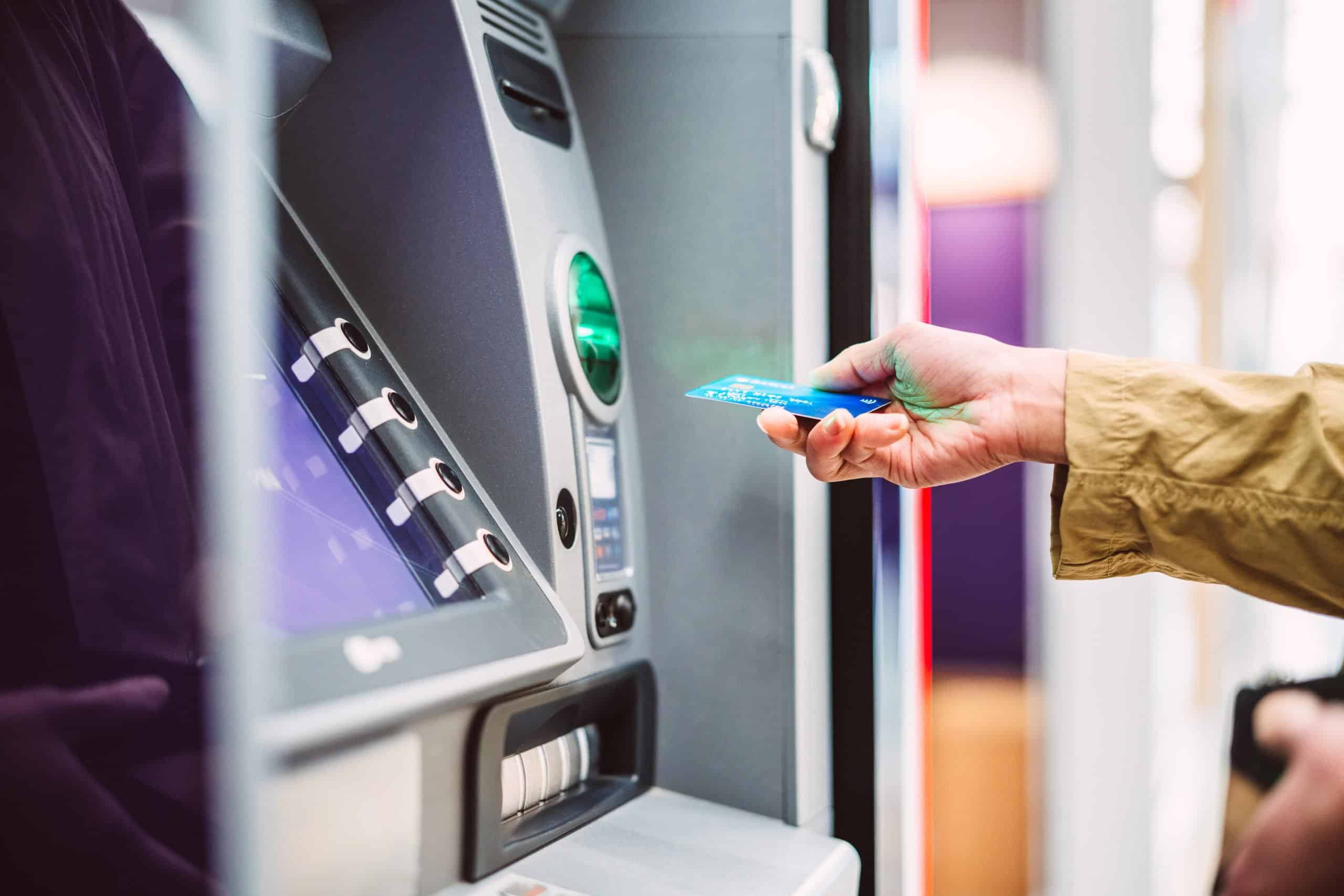 | Female hand inserting bank card into automatic cash machine (ATM) to access bank account services in the city