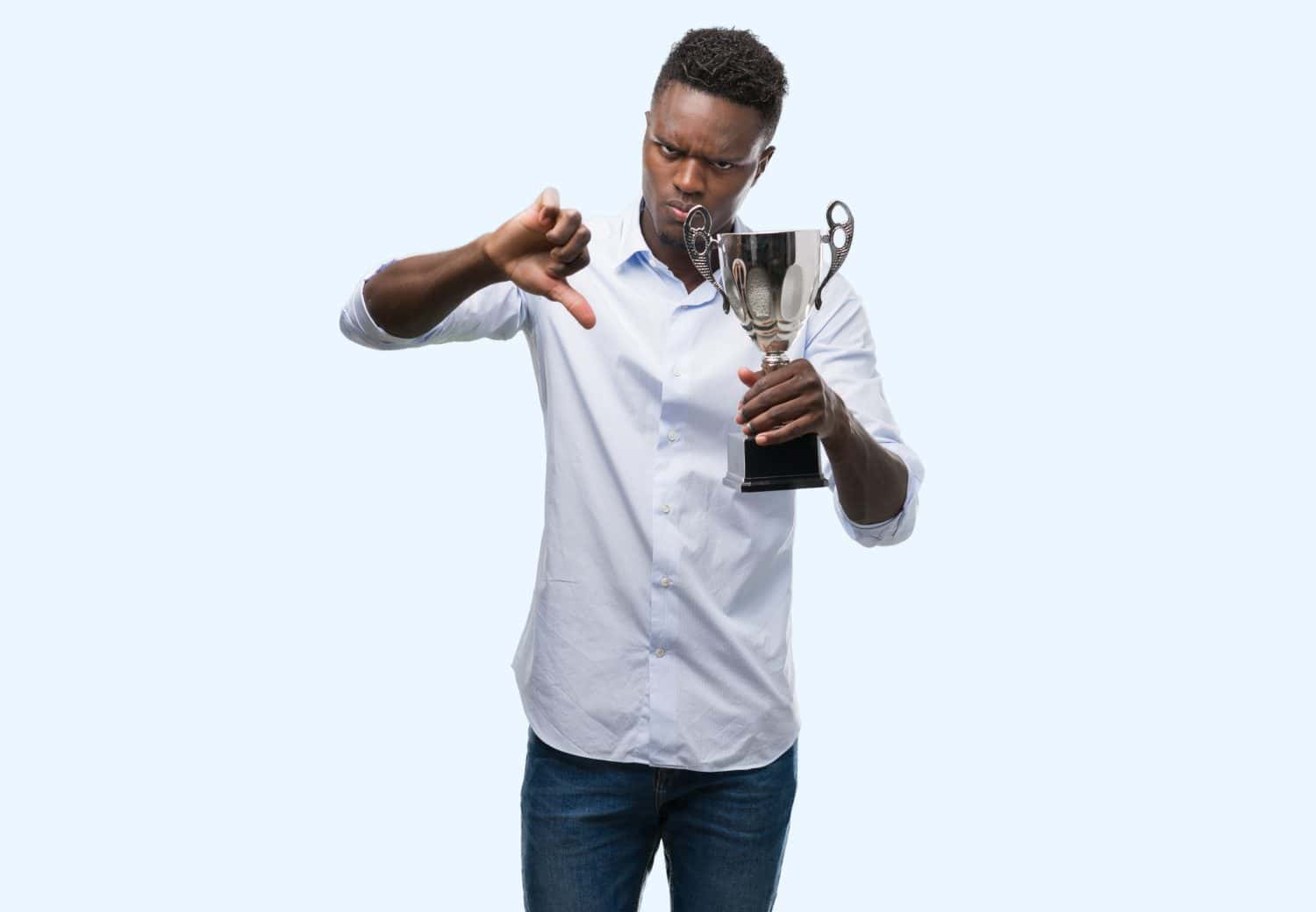 Young african american man holding trophy with angry face, negative sign showing dislike with thumbs down, rejection concept