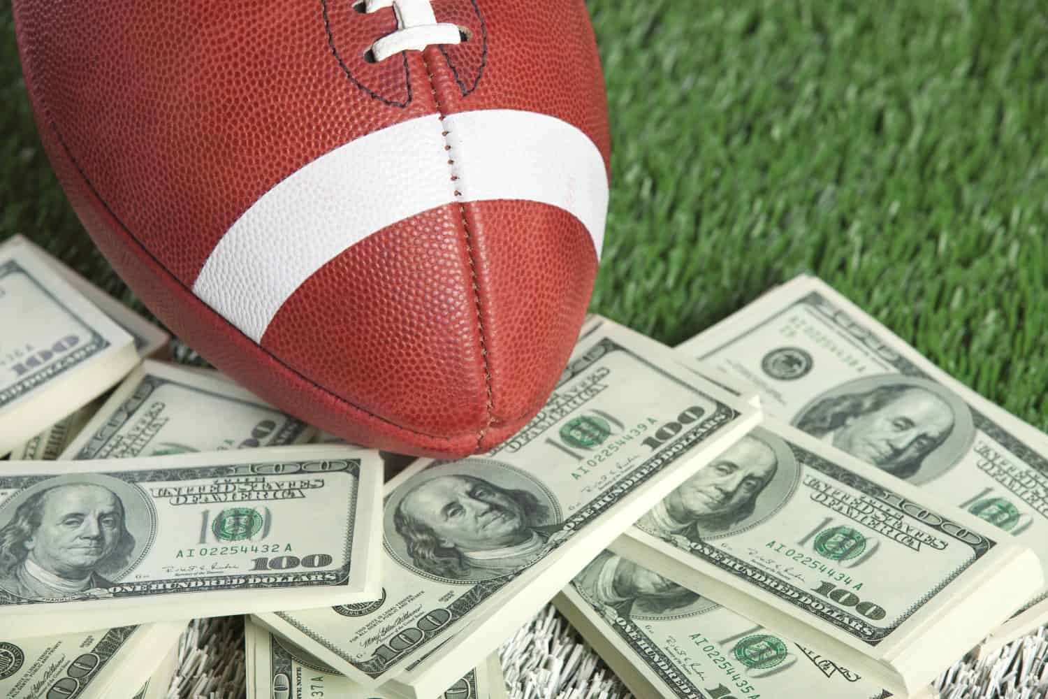 A college style football sits with a pile of money on a green field