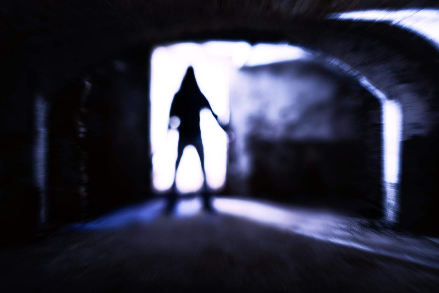 Silhouette of evil theatening body in dark basement - Sinister figure standing at dungeon door with dangerous attitude - Concept of a dreadful encounter with blurred subject in backlight - Image