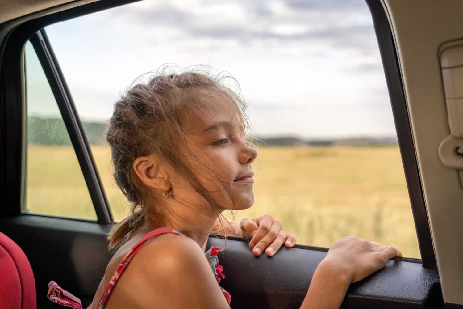 Beautiful little girl looking through window and enjoying freedom of car journey at sunset.