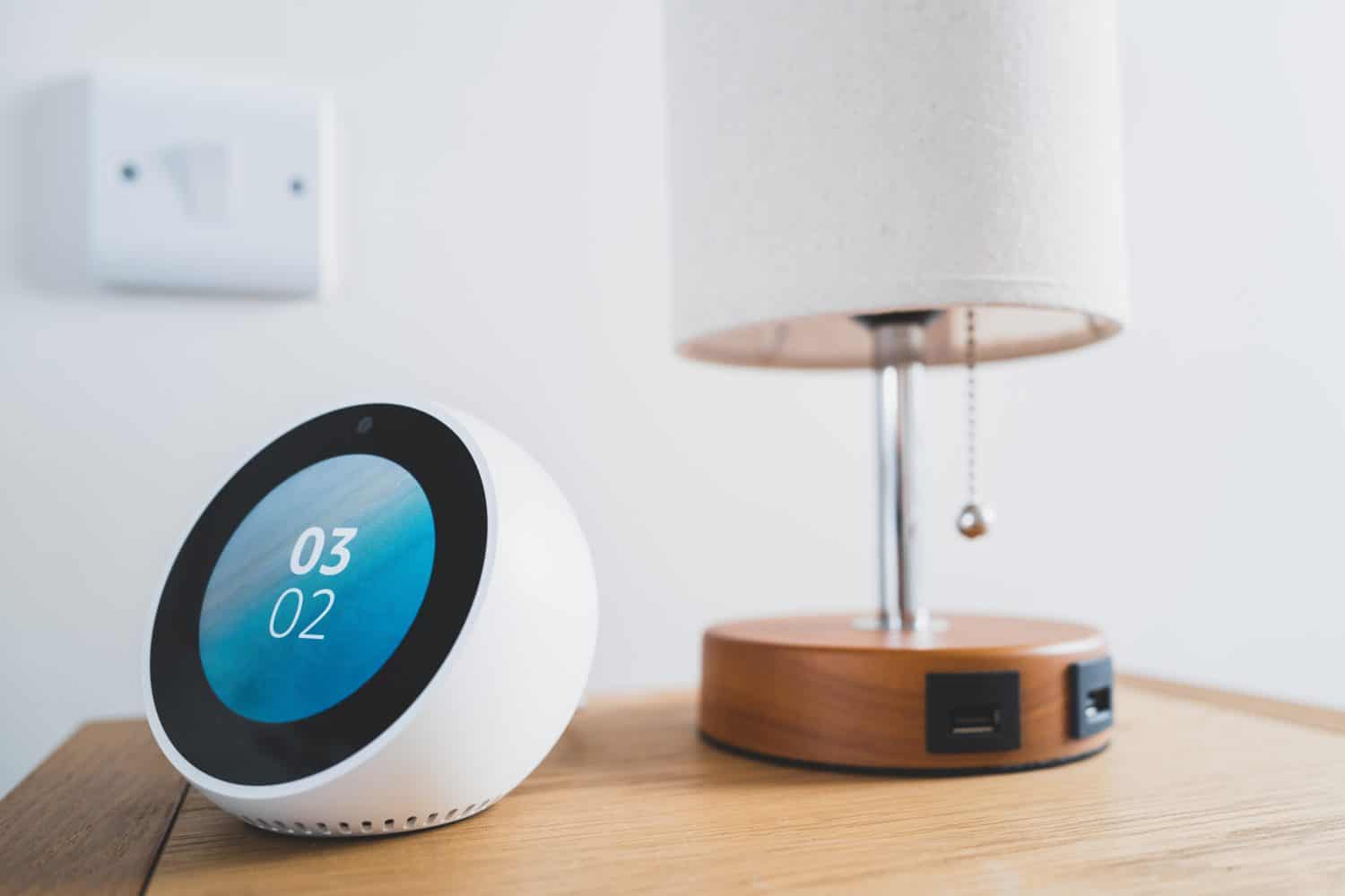 Bedside smart device showing the local time. Located next to a beside lamp with USB charging ports.