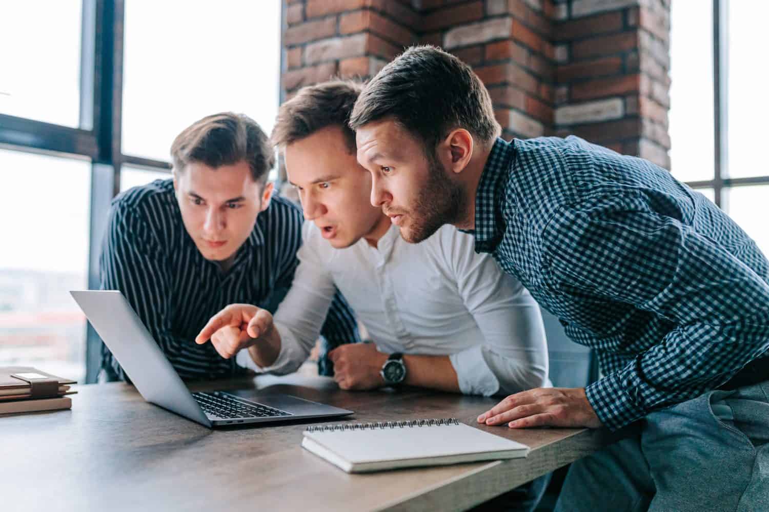 Three young men in an office, staring in amazement at their laptop screens. The work in front of them seems to have left them flabbergasted and bewildered.