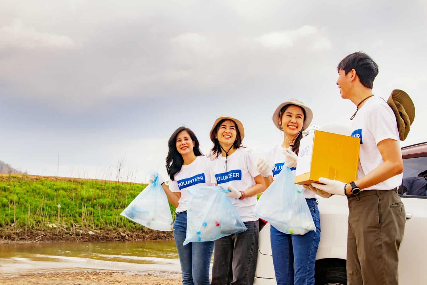 Male volunteers holding donation boxes and dividing into groups female teams holding garbage bags during doing good deeds nature conservation project volunteers tourism areas natural water resources.