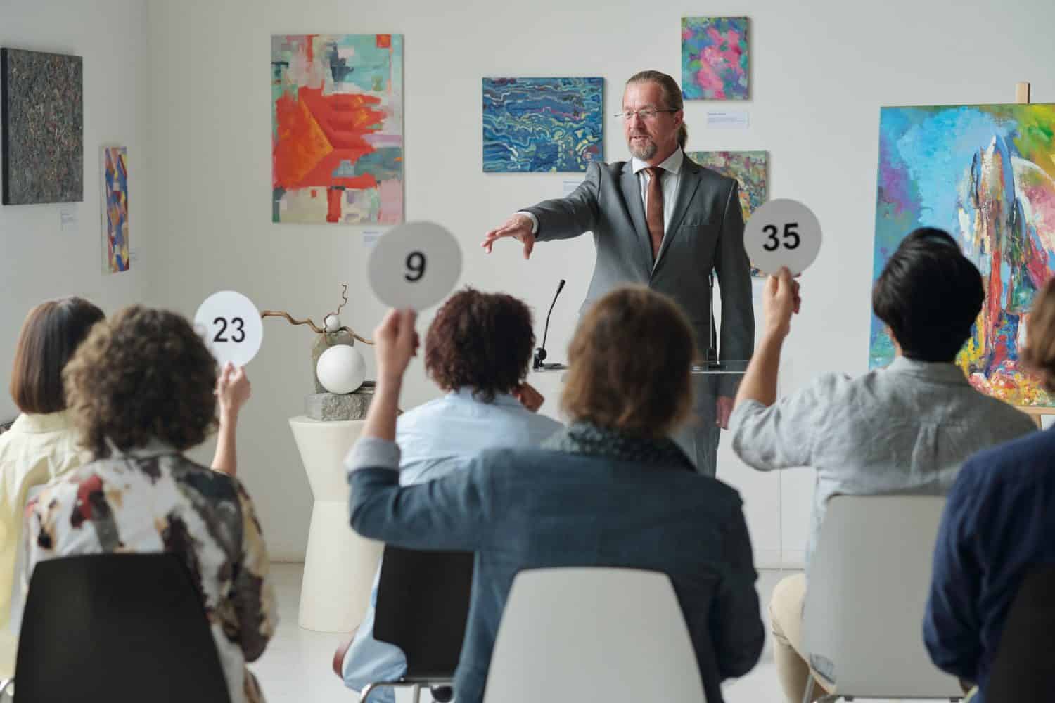 Group of people raising tablets with numbers up while sitting at auction in art gallery