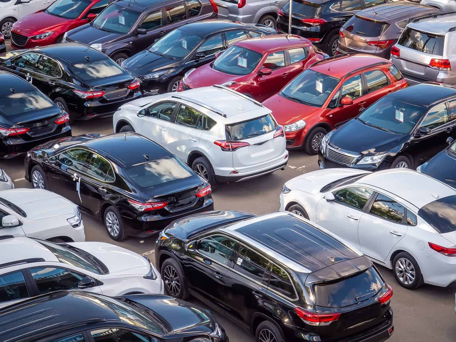 Sale of new and used cars in a dealership. Lots of cars in the car park. Black, white, silver and red cars of unknown brands