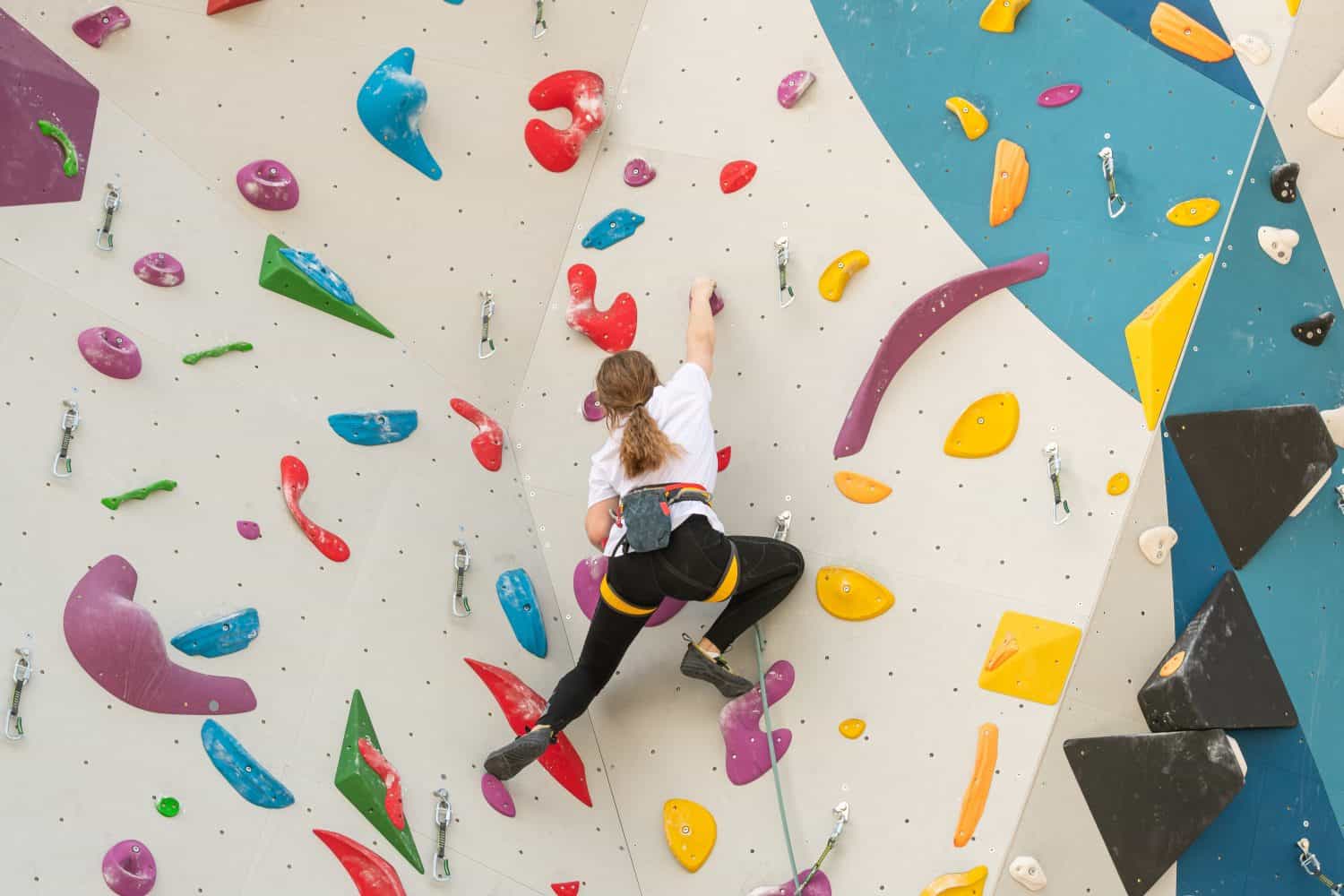 The climber climbs the artificial stone wall with the help of safety belts. An active young woman on a stone wall in a sports center. A girl trains on a rock climber in the open air.