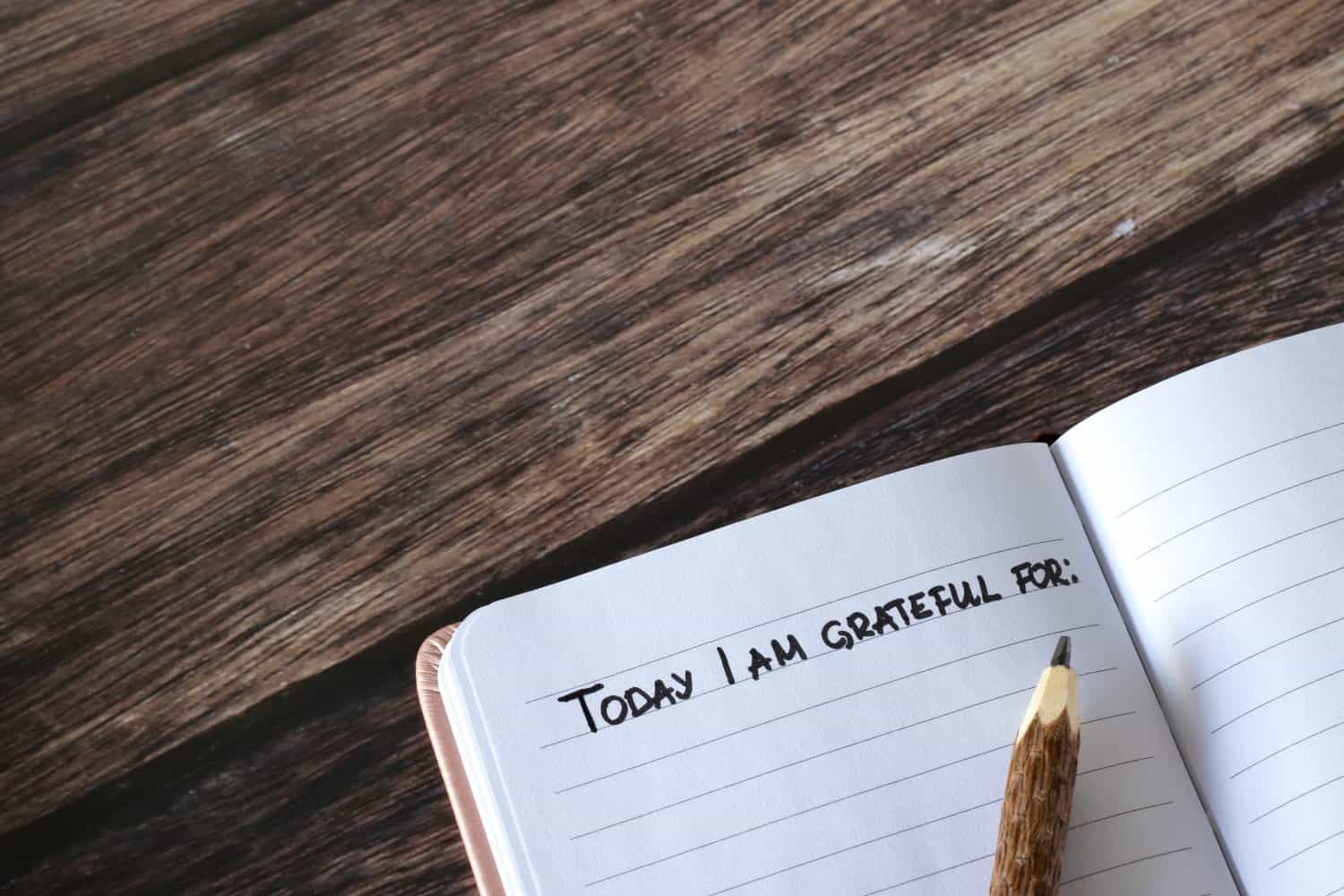 Open journal with handwritten text for gratitude and thanksgiving and pencil on wooden table. Top view, copy space. Giving thanks to God Jesus Christ for blessings in personal notebook.