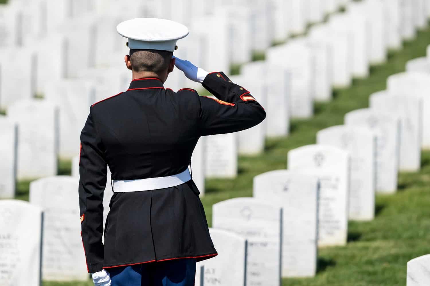 A poignant moment unfolds as a Marine plays taps, honoring a fallen veteran with a solemn salute, marking their internment at a national military cemetery.