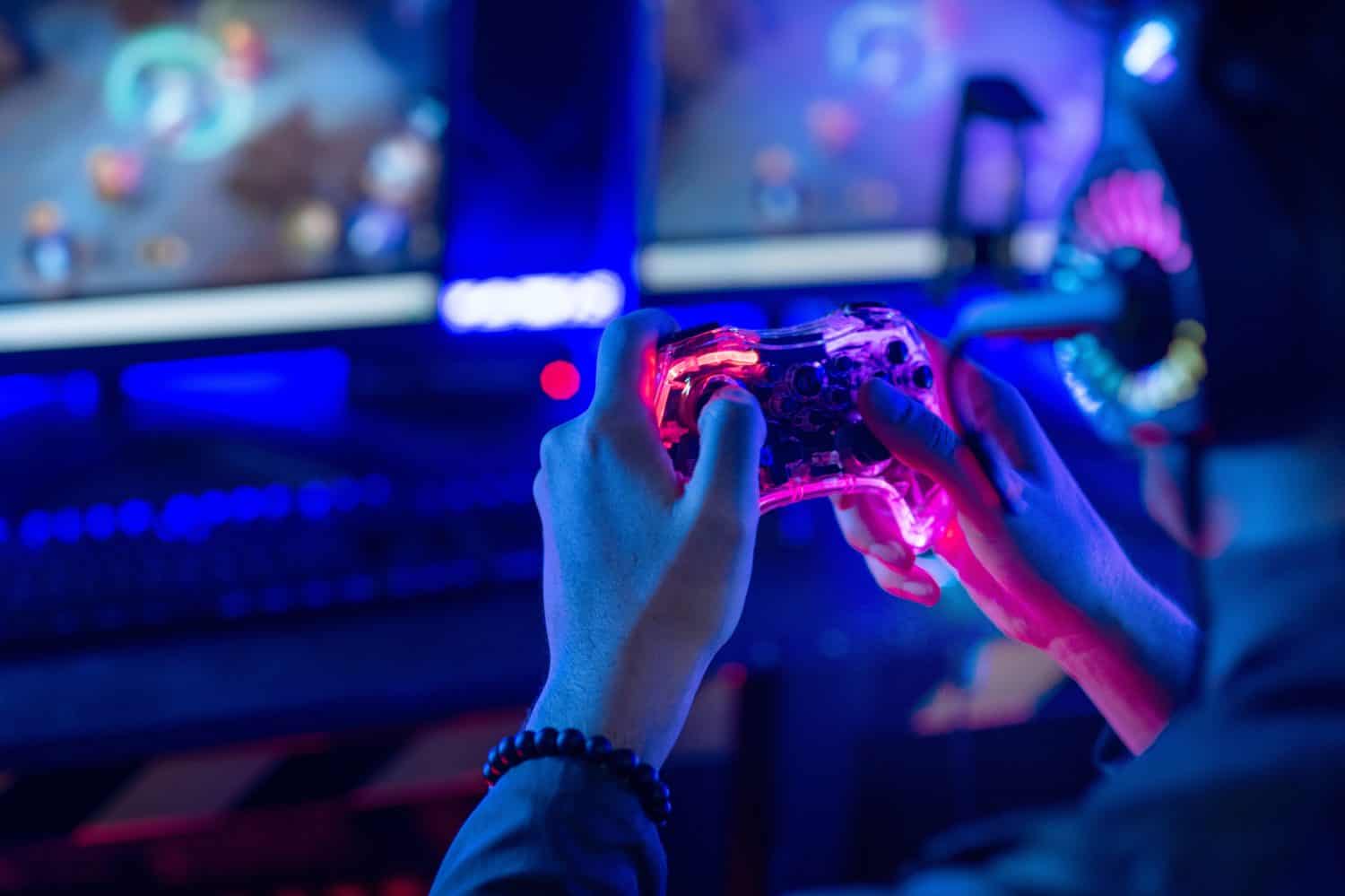 Close-up, video game console controller in gamer hands at colorful neon light living room at night, E-sport streaming game online, selective focus