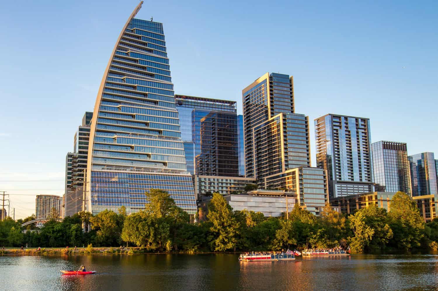 Modern architecture and high-rise buildings of Austin, Texas with summer sunlight reflections on Lady Bird Lake. A ground-level view of the lake and boats on the water.