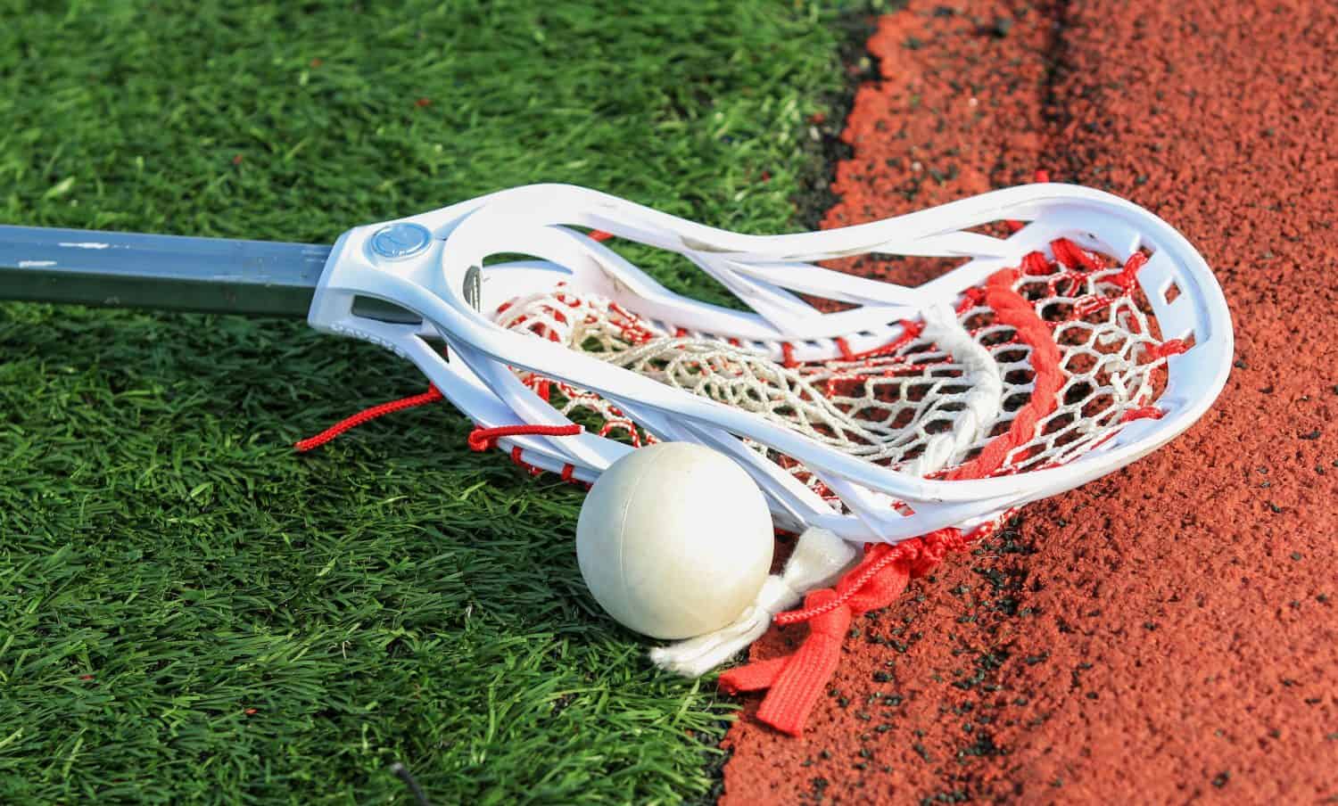 Lacrosse stick on the turf next to a ball close to a red track