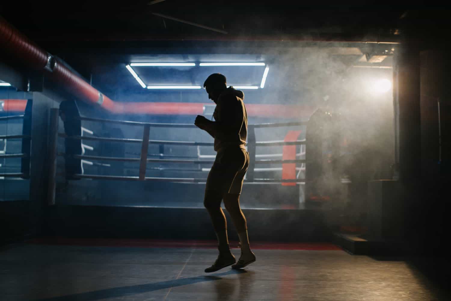 A male boxer is boxing with a shadow on the background of a boxing ring. A boxer practices his punches in a boxing studio.