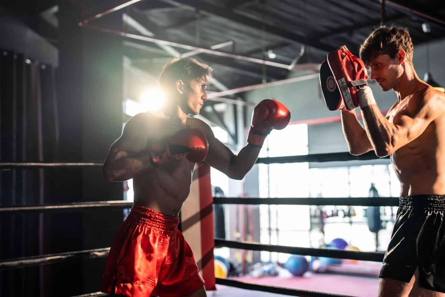 Two young professional boxer having a competition tournament on stage. Attractive male athlete fighters muscular shirtless punches and hitting competitor enjoy boxing exercise in the ring at stadium.