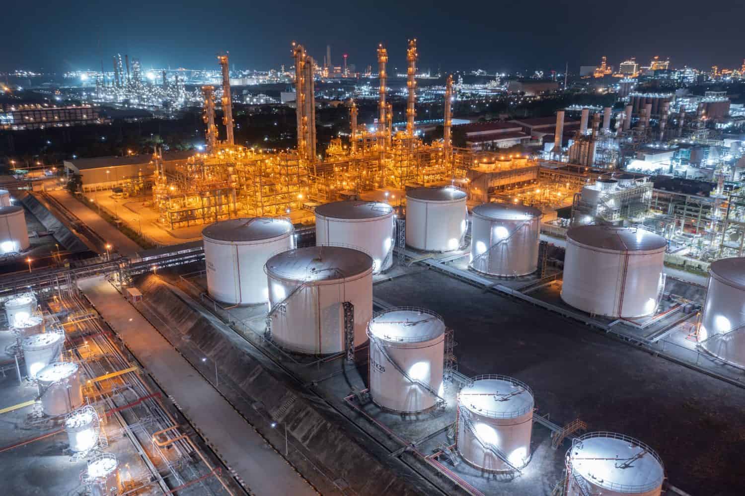 Glowing storage tanks and a labyrinth of pipes define an oil refinery under the cover of darkness, a testament to continuous industrial activity.