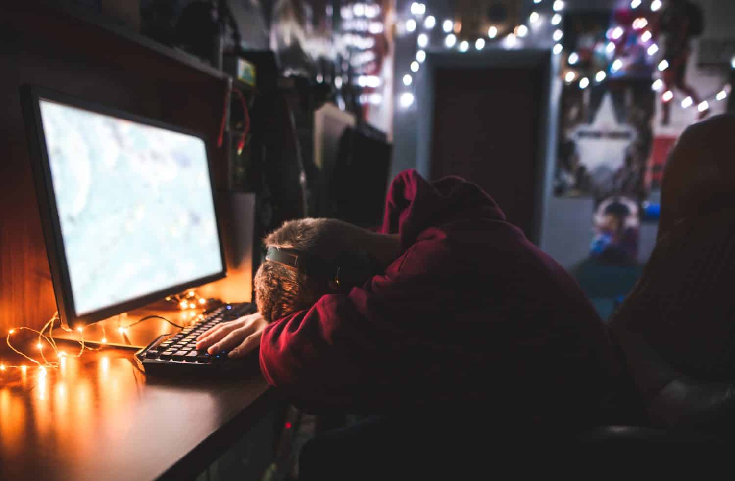 Gamer sleeps on the desk for a computer game. Portrait of a frustrated gamer near a computer. Tired teenager fell asleep while playing on a computer. Video Games