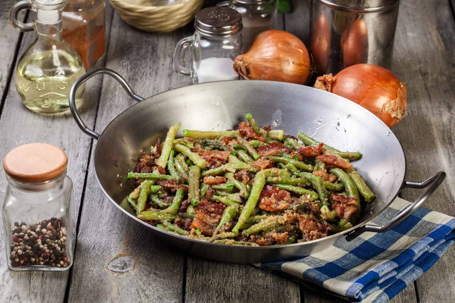 Healthy sauteed green beans with bacon, onion, and bread crumbs on steel frying pan