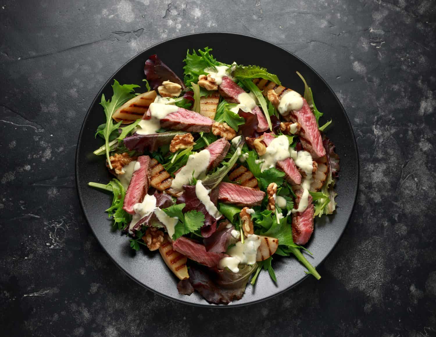 Grilled Beef Steak salad with pears, walnuts and greens vegetables and blue cheese sauce. healthy food.