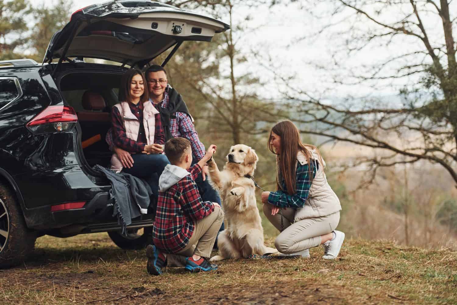 Happy family have fun with their dog near modern car outdoors in forest.