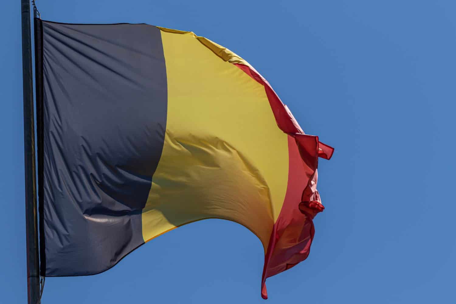 Belgian national flag waving on blue sky background. Kingdom of Belgium, BE