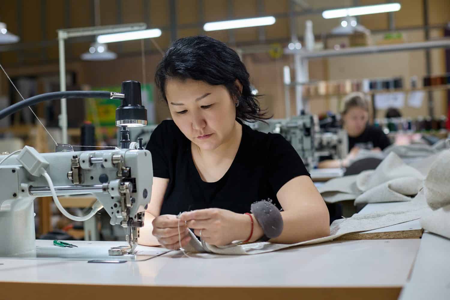 Seamstress or an employee of an Asian textile factory sewing on an industrial sewing machine. The process of sewing from fabric