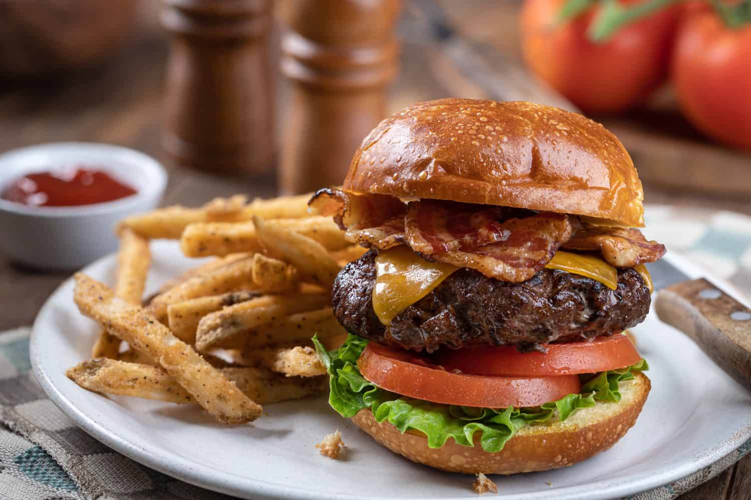 Bacon cheeseburger with lettuce and tomato on a toasted bun and french fries on a plate