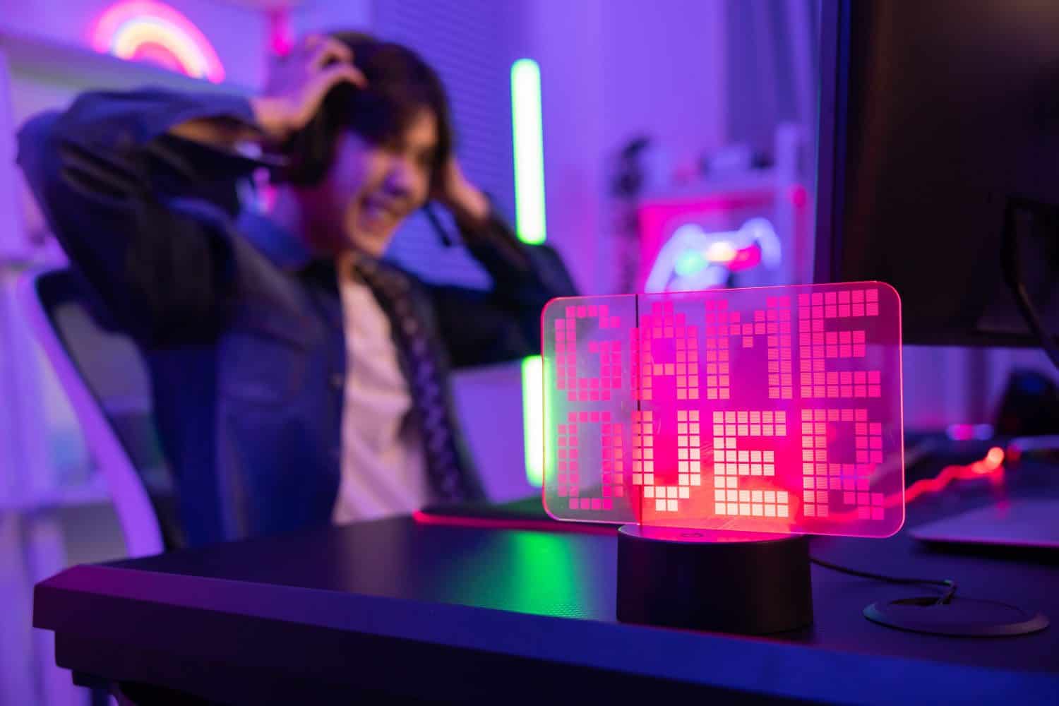 View of Game Over Neon Sign with Blurred Upset Gamer Losing the Game