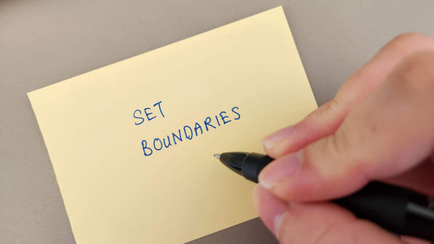 A hand holding a pen, pointing at the words Set Boundaries written on a sticky note