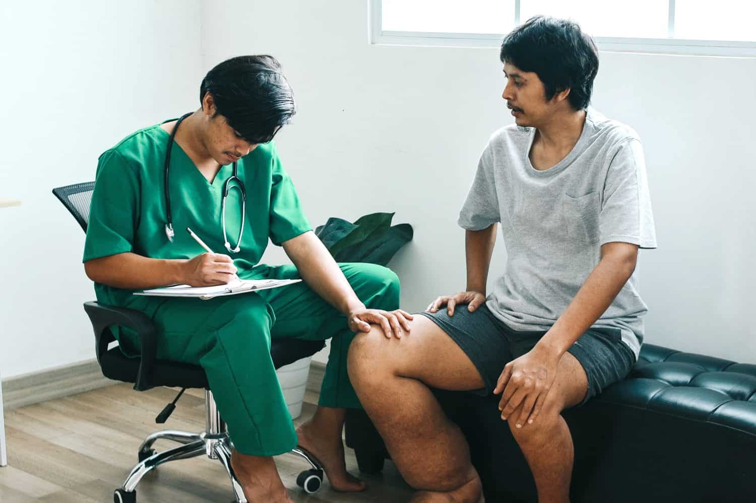 Doctor listening to the complaints health patient that suffering from elephantiasis while making notes in clipboard