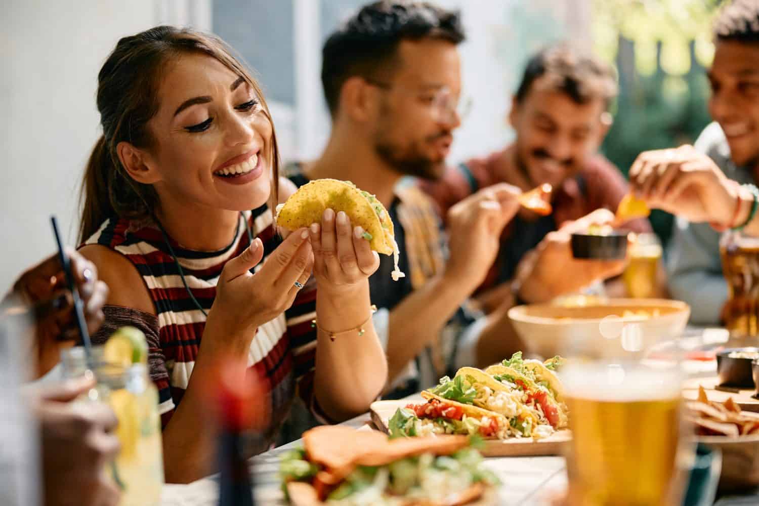 Young woman enjoying in a taste of tacos while having lunch with friends in restaurant.