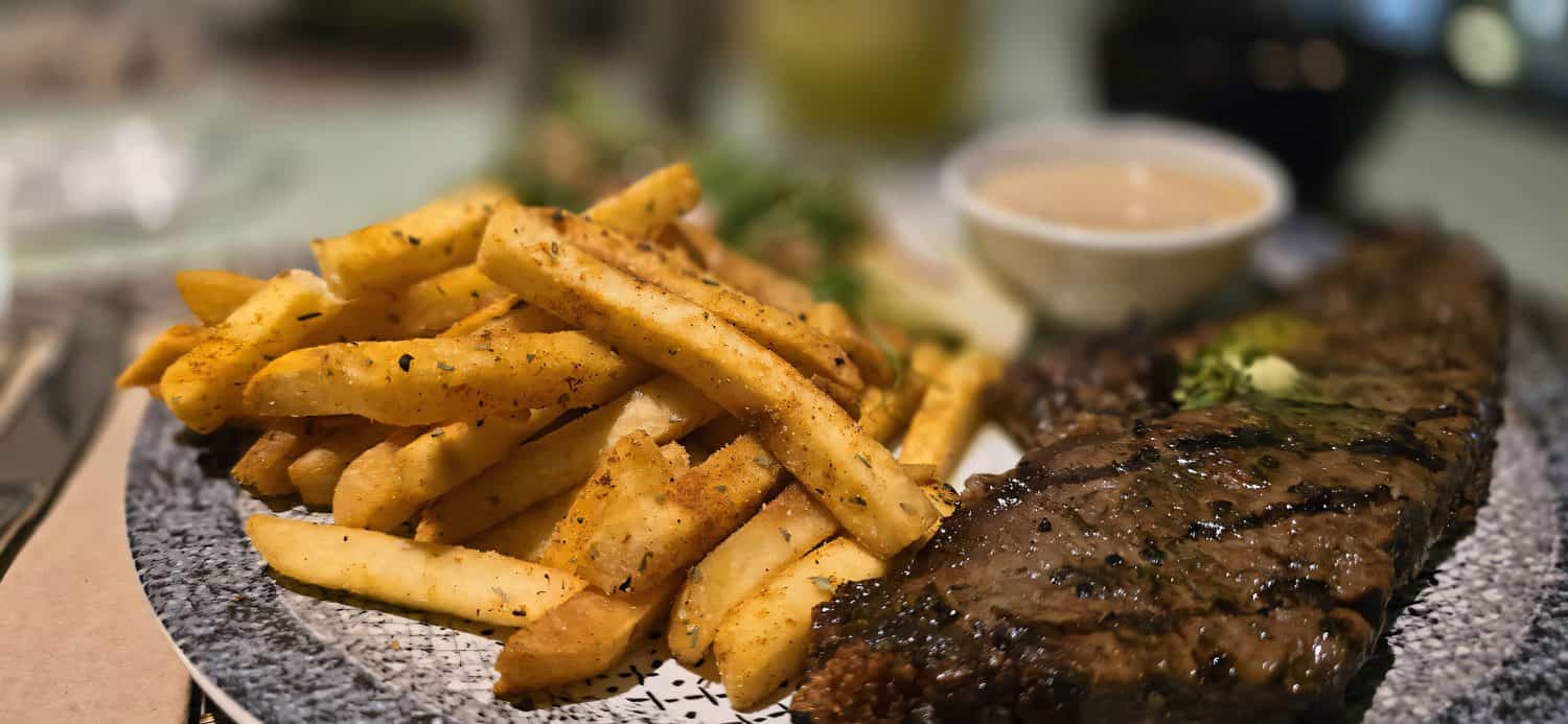 Sirloin steak grilled medium rare served with potatoes and salad with mushroom black pepper sauce in a restaurant