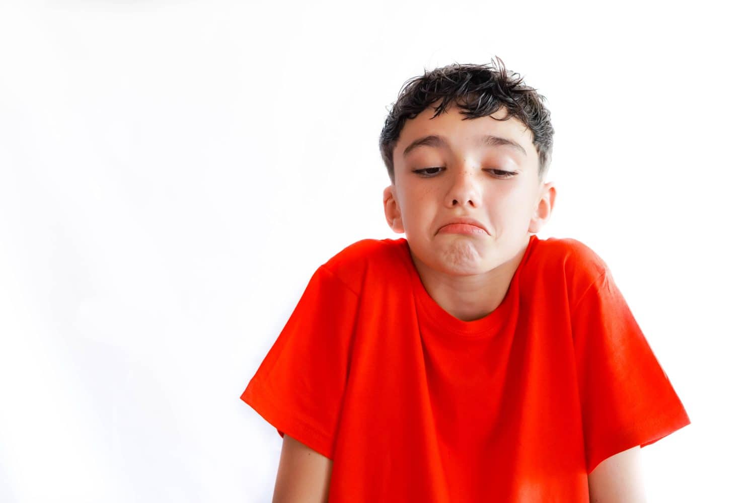 preteen boy gesturing i don´t know, doubt or indifference. white background and red t-shirt.