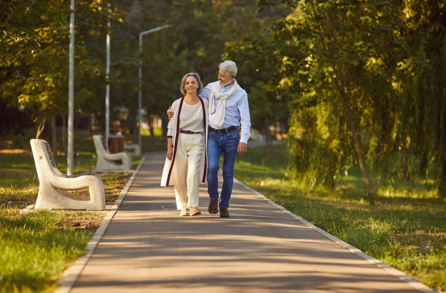 Senior couple, wife and husband, walking hand in hand in a city park, enjoying vacation or holiday together. They are active and happy, savoring leisure time, strolling and talking outdoors.