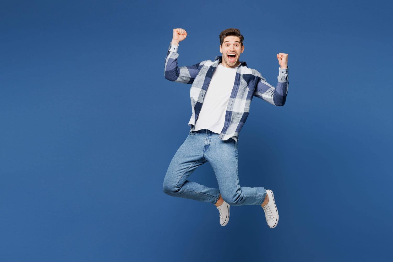 Full body young happy man he wear shirt white t-shirt casual clothes jump high doing winner gesture celebrate clenching fists isolated on plain blue cyan background studio portrait. Lifestyle concept