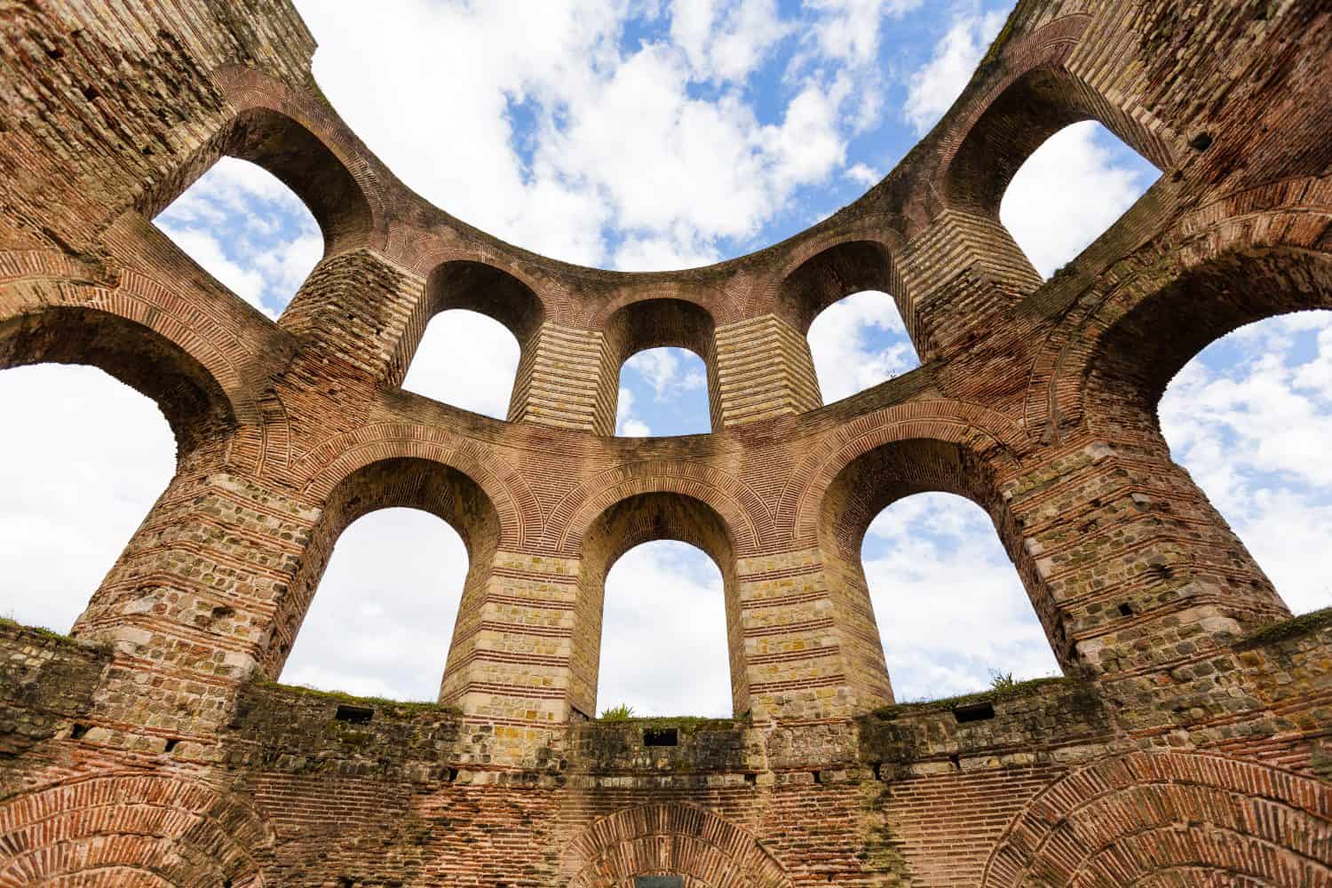 Trier imperial Roman bathhouse ruin with arches, against a blue sky with clouds